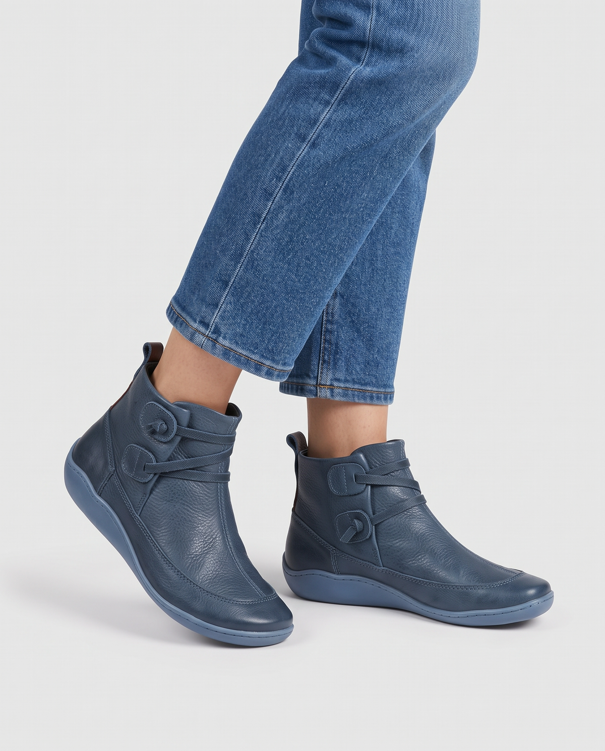 Women's soft leather ankle boots with a criss-cross strap and two button tabs on the side, back pull tab and flexible wavy sole in Blue, front view